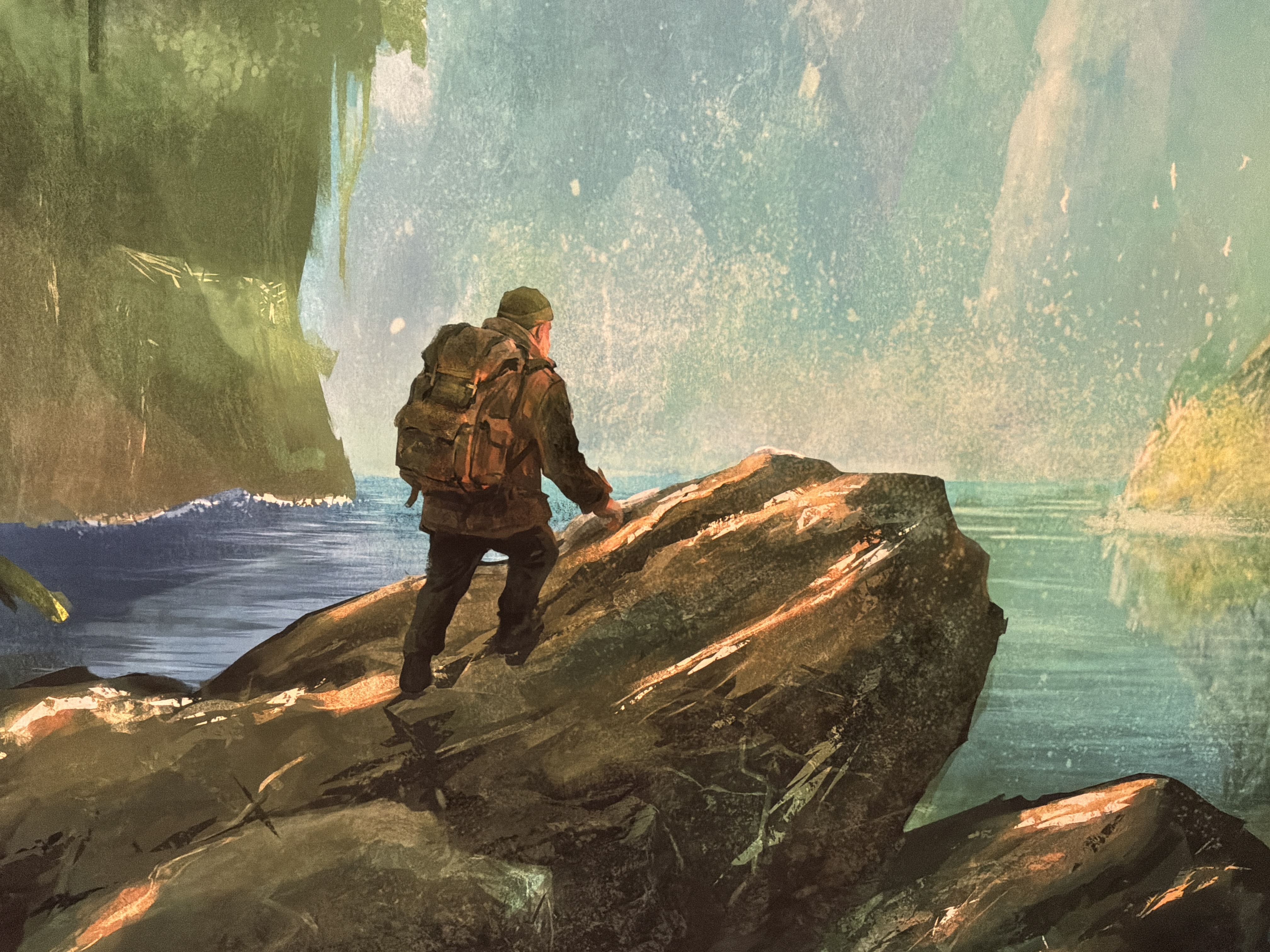 Hiker with a large backpack stands on jagged rocks by the sea, looking toward the water.